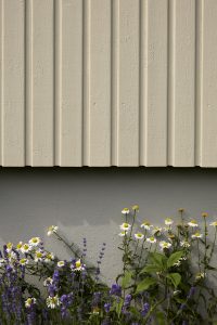 Utsnitt av beige trevegg utendørs malt med JOTUN DRYGOLIN Sandbeige, grunnmur i gått malt med